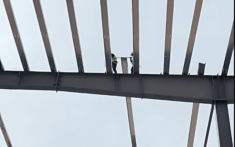 Construction workers installing steel roof panels on a structural frame.