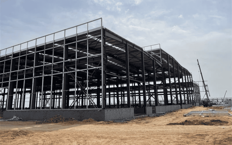 A large-scale steel structure under construction, showcasing beams, columns, and the roof framework.