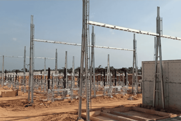 An electrical substation under construction with steel frameworks and concrete foundations on a sandy site.