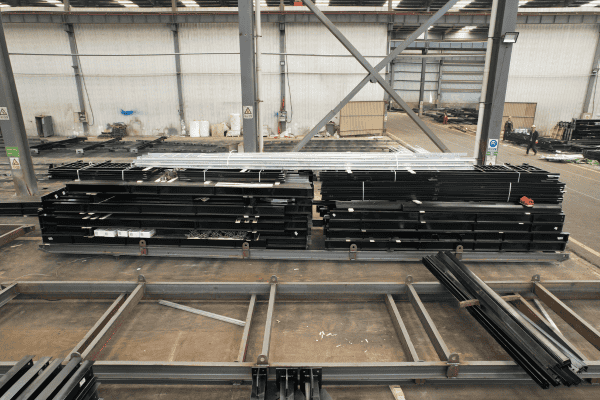 Prefabricated black steel beams stacked neatly in a warehouse for assembly or shipment.