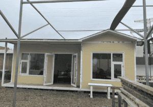 A single-story yellow prefab house with open glass doors and windows, showcasing a cozy and functional design, placed outdoors.