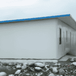 A white prefab house with a blue roof and simple design, placed on a rocky surface, demonstrating efficient and durable construction.