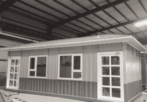 A single-story Temporary Modular Building with metallic siding, multiple windows, and glass-paneled doors, situated inside an industrial shed.