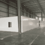 A long, white Temporary Modular Building with small windows, placed inside a large industrial warehouse. A car is parked nearby.