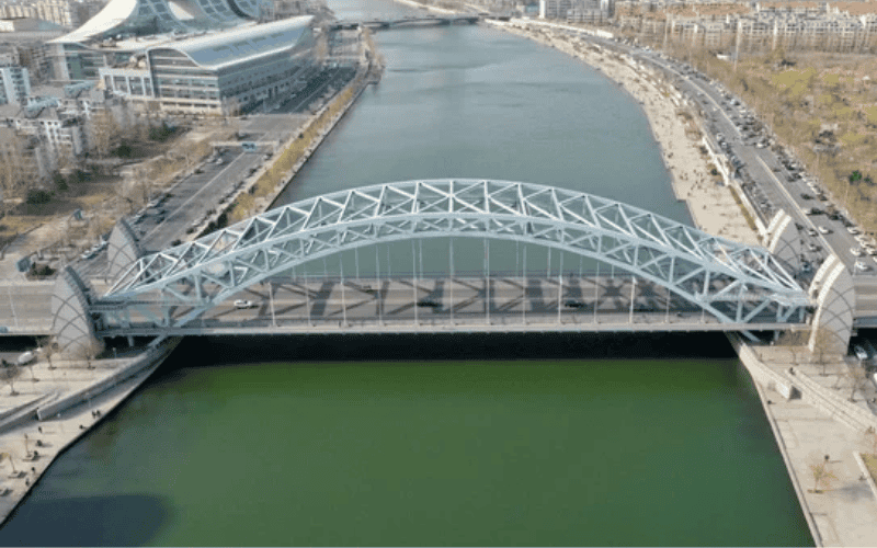 "Aerial view of a steel arch bridge spanning a river in an urban area."