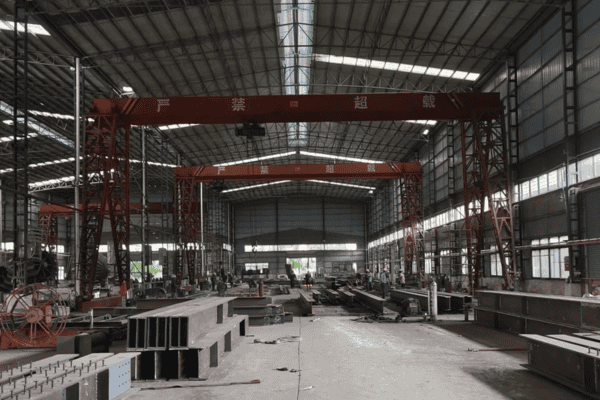 An industrial workshop with large steel components, overhead cranes, and a spacious interior.