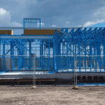 The blue steel structure frame is under construction and the site is fenced off. Steel components have quality assurance for durability and long-term performance.