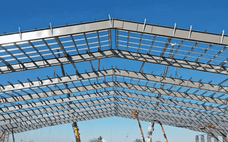 Steel frame structure of an office building under construction against a blue sky.