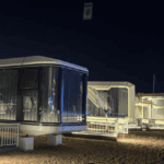 Night view of several illuminated prefab houses with large glass windows and futuristic design.