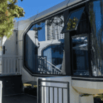 Bright daytime photo of a prefab house with large windows and a modern entrance, surrounded by trees.