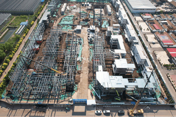 An aerial view of an industrial steel structure construction site with cranes and prefabricated buildings in progress.