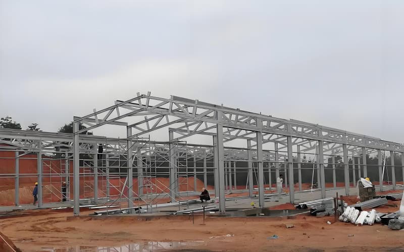 A large steel - framed structure under construction, separate from the chicken coops shown.