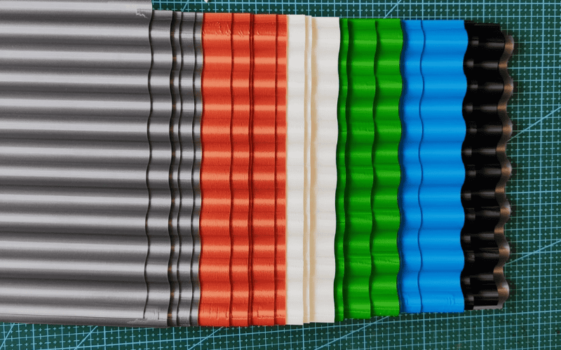 A variety of corrugated metal sheets in multiple colors, including silver, red, green, and blue, displayed on a cutting mat background.