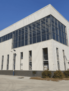 Exterior view of a modern steel structure building with large glass windows and a clean white facade under a clear blue sky.