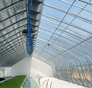 A modern greenhouse-style metal barn with a curved transparent roof, insulation, and a hydroponic planting system inside.