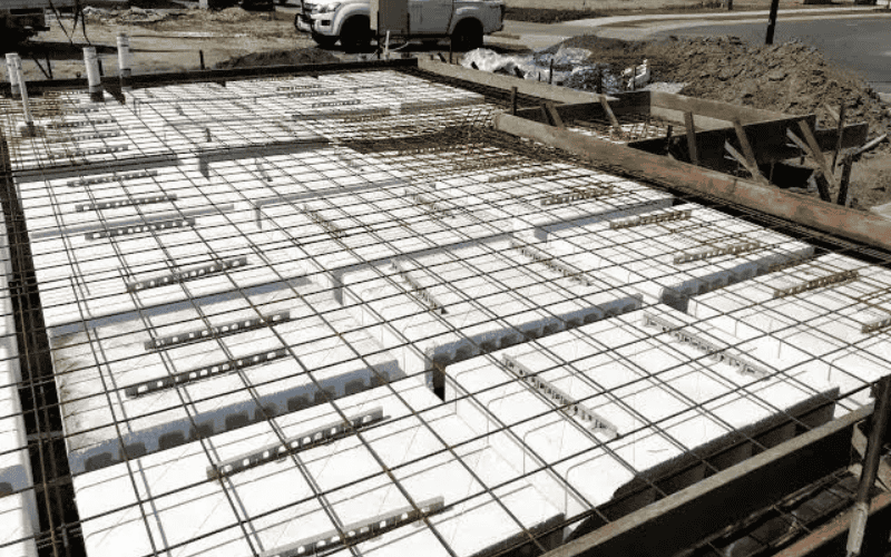 Close-up view of a concrete foundation with a rebar grid and polystyrene blocks placed for insulation and structure.