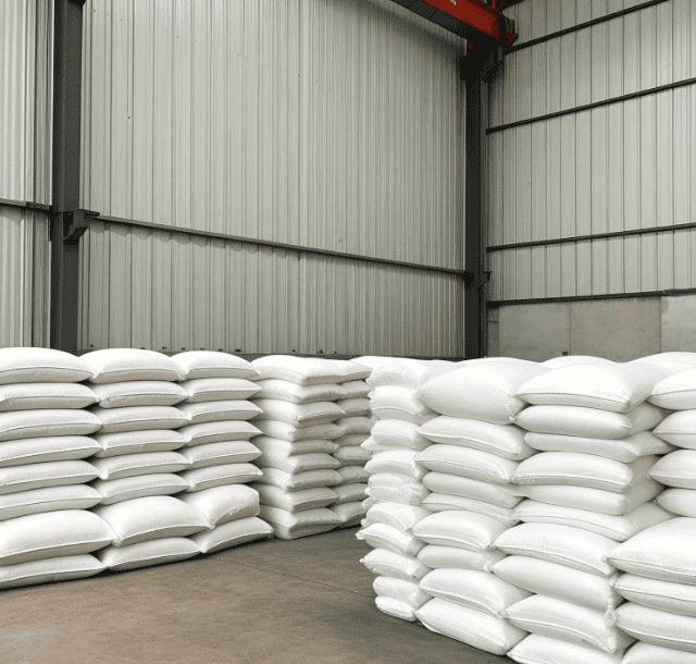 A modern steel barn storing neatly stacked white bags of salt, in an organized manner with a high ceiling and steel siding.