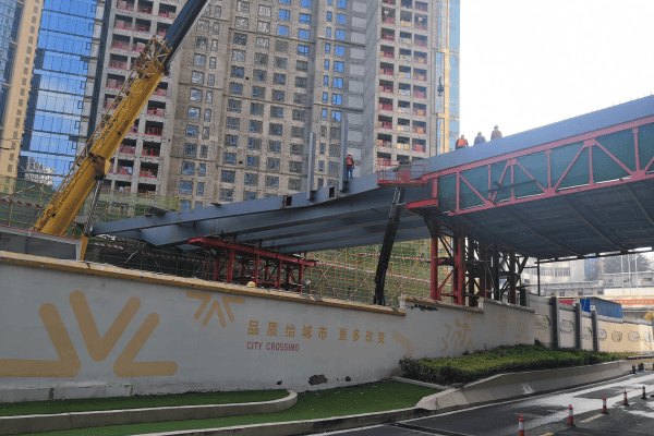 A construction site featuring a steel beam installation for a modern city overpass with high-rise buildings in the background.