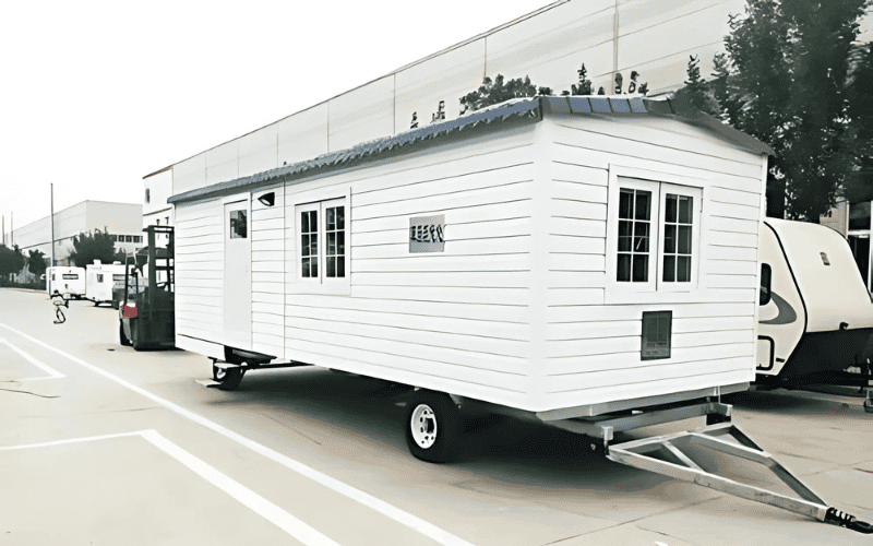  A white modular home being transported on a truck, featuring a simple design with windows and a roof, indicating the mobility of modular units.