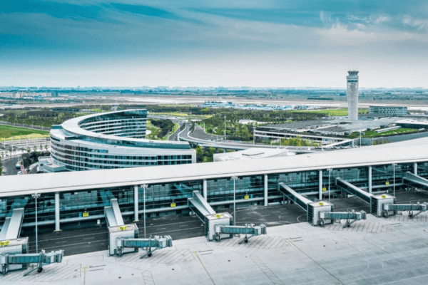 A modern airport terminal with a curved glass facade, air bridges, and a control tower in the background.