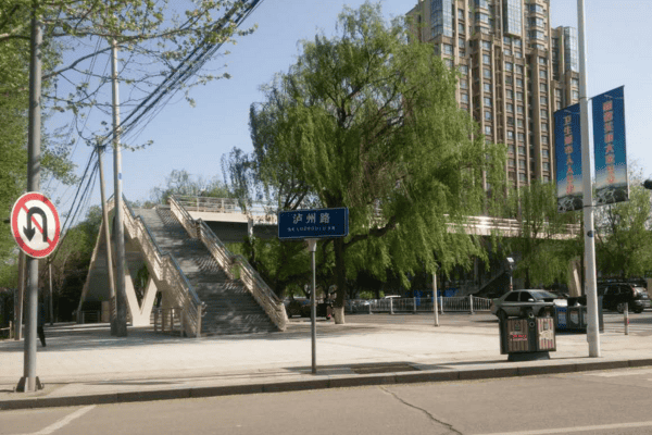 A staircase leading to a pedestrian bridge in an urban area, surrounded by trees and tall apartment buildings.