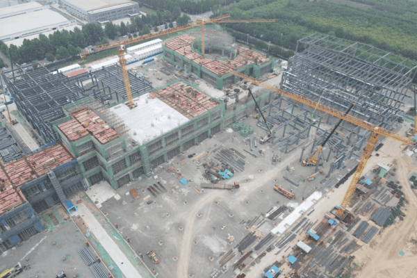 An aerial view of a large logistics construction site with steel frameworks, cranes, and materials organized on the ground.