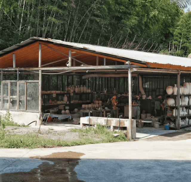 A metal lean-to barn converted into a pottery workshop, featuring open walls, shelves with ceramic pots, and a natural backdrop.