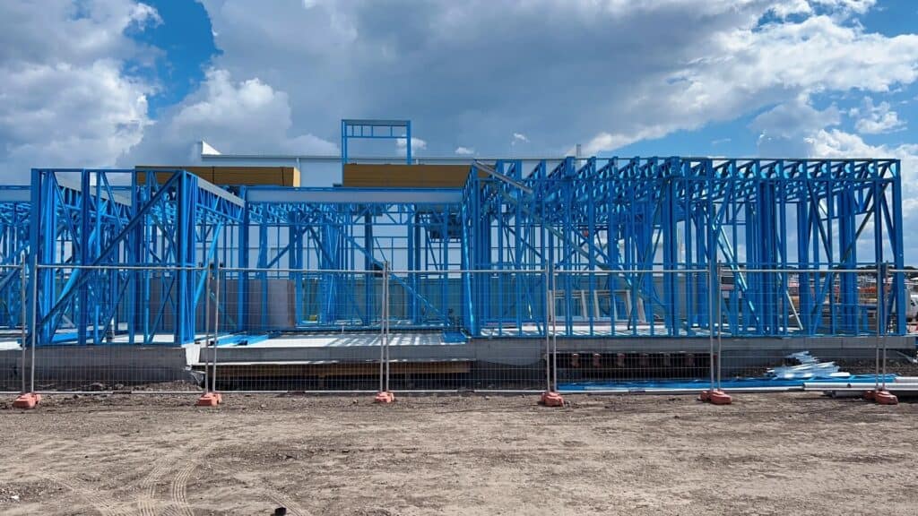 A light gauge steel structure under construction, featuring blue - hued framing and set against a cloudy sky.