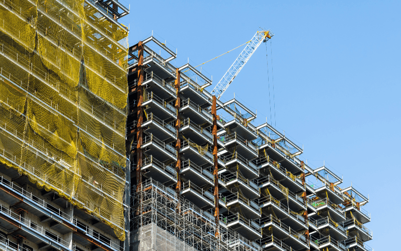 A close-up of a light steel structure used in residential construction, showing steel beams, scaffolding, and the process of constructing a multi-story building.