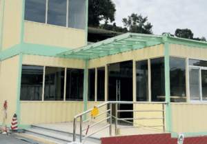 A modular lunchroom with a yellow and green exterior, large windows, and a glass canopy entrance, designed for a modern and functional dining space.