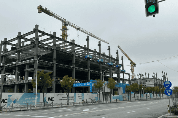 A steel frame building under construction with cranes and safety barriers on a cloudy day.