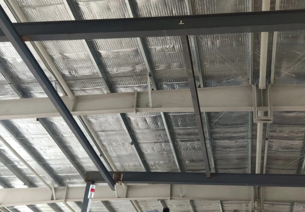 An overhead view of an Enclosure System in a Peb Structure, showing metallic insulation panels and steel beams, for thermal insulation and protection.