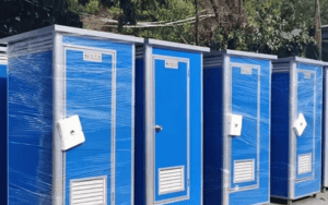 Blue portable restroom units, wrapped in protective plastic, lined up in an outdoor setting.