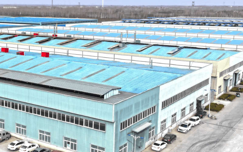 An aerial view of a large industrial complex with blue corrugated steel roofing and multiple factory units.