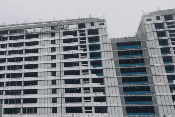 A partially constructed hospital building with a modern facade and exposed steel framework under a gray sky.