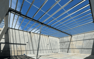 A steel frame structure under construction with a clear blue sky, featuring horizontal beams and vertical supports, designed for a modern industrial facility.