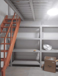 Interior view of a steel mezzanine with orange stairs, grey shelving, and installed structural components.