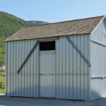 A white metal barn with a peaked roof, large doors, and a clear sky background.