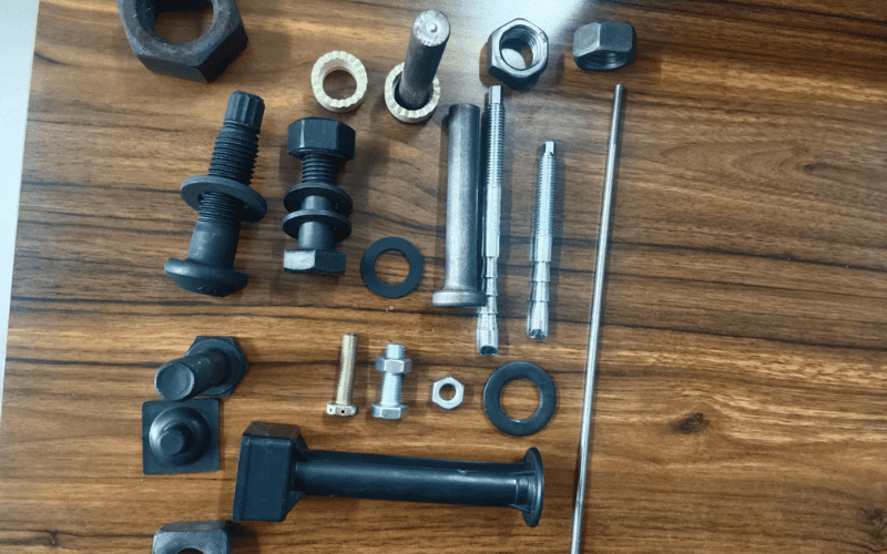 Assorted bolts and fasteners arranged on a wooden table, emphasizing their applications in steel structures.