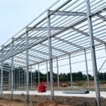 Expansive steel structure framework of a poultry building under construction, with construction equipment and materials on the concrete - paved ground.