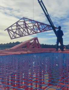 A crane lifting steel trusses for a roof structure during construction on-site.