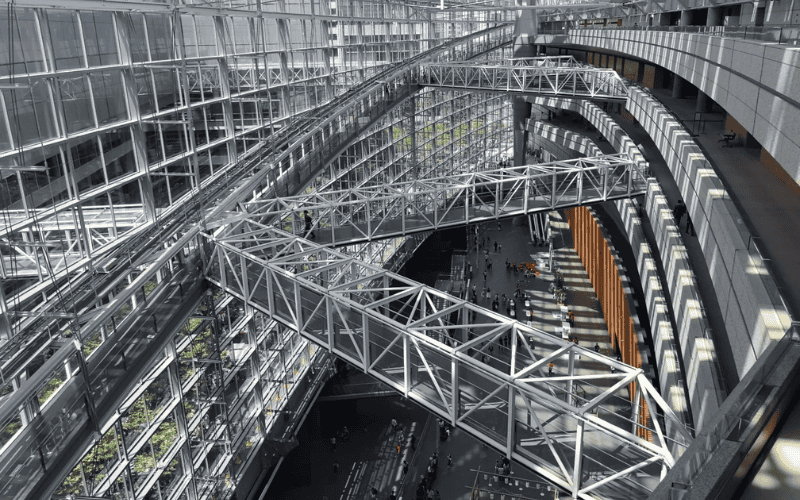 A large atrium with steel trusses and glass walls, featuring pedestrian bridges connecting different sections of the building.