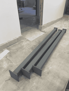 Three grey-painted steel columns placed on a concrete floor, prepped for installation.