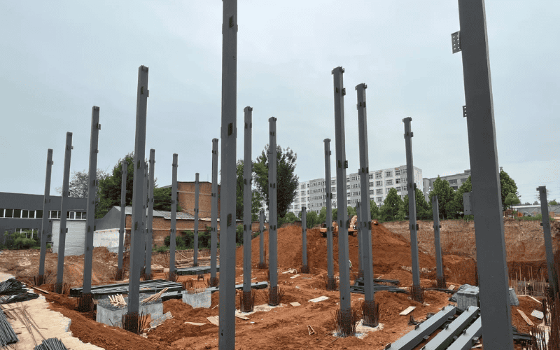 Construction site with multiple vertical steel columns installed on concrete foundations.