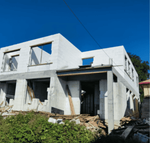 Ein teilweise fertiggestelltes Gebäude aus weißen Blöcken mit offenen Fensterflächen und verstreuten Baumaterialien auf der Baustelle.