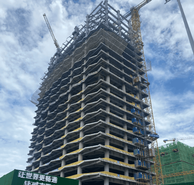 A tall building under construction with visible steel structure framework, cranes, and construction workers in the process of building the high-rise.