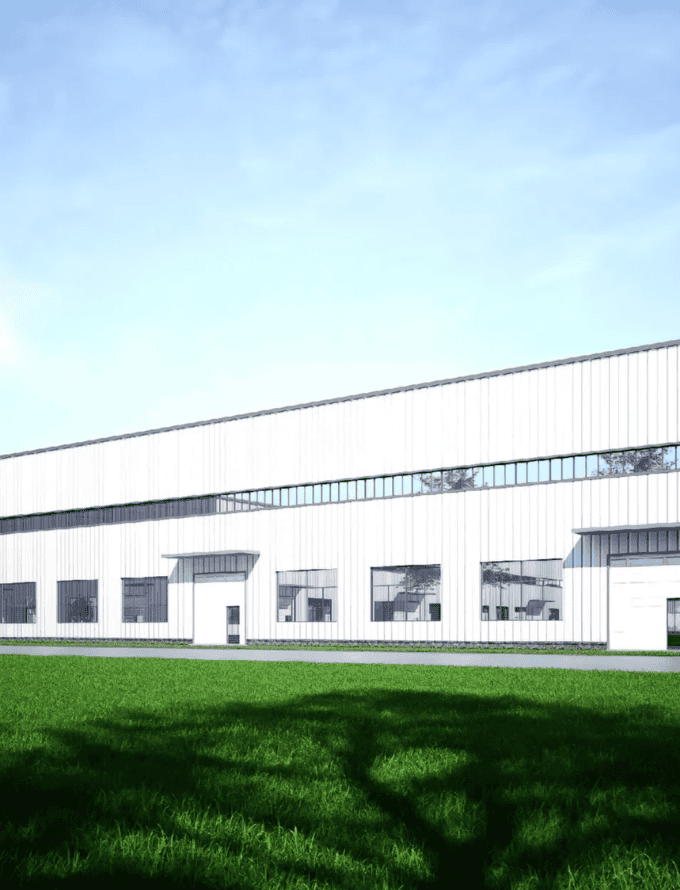 Modern steel structure warehouse with white exterior walls and large windows, surrounded by a green lawn under a clear blue sky.