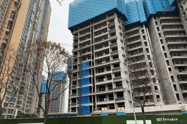 A high-rise residential building under construction with scaffolding and blue protective coverings.