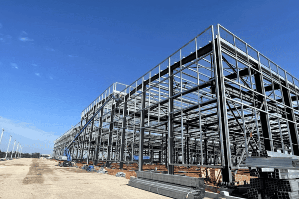 A large steel frame structure under construction, set against a clear blue sky.