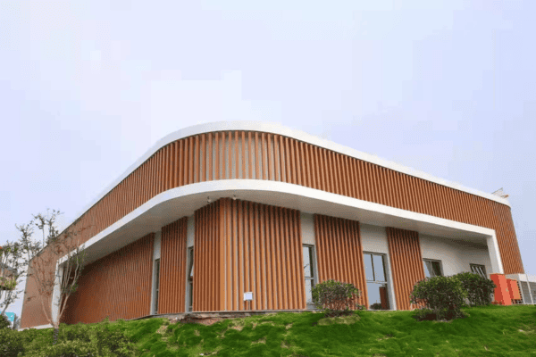 A curved, modern building with a brown vertical panel facade, set on a landscaped green lawn.